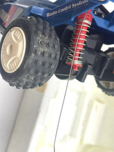 Load image into Gallery viewer, Close-up of car suspension featuring large tires and red springs.
