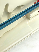 Load image into Gallery viewer, Detail of a cream container with blue stripe and red accents.
