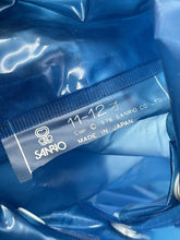 Carica l'immagine nel visualizzatore di Gallery, Detail shot of the size label on the blue Hello Kitty raincoat.
