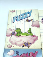 Carica l'immagine nel visualizzatore di Gallery, Detail close-up of a notebook cover featuring a cartoon dinosaur against a cloud background.
