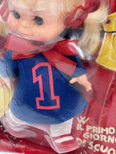 Carica l'immagine nel visualizzatore di Gallery, Detail view of the doll wearing a number 1 shirt and pigtails in plastic packaging.
